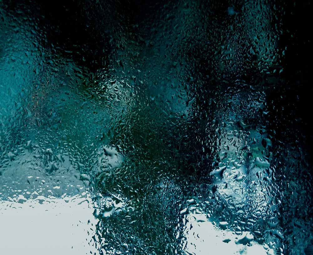 blue and green reflecting on glass that has condensation and rain drops on it