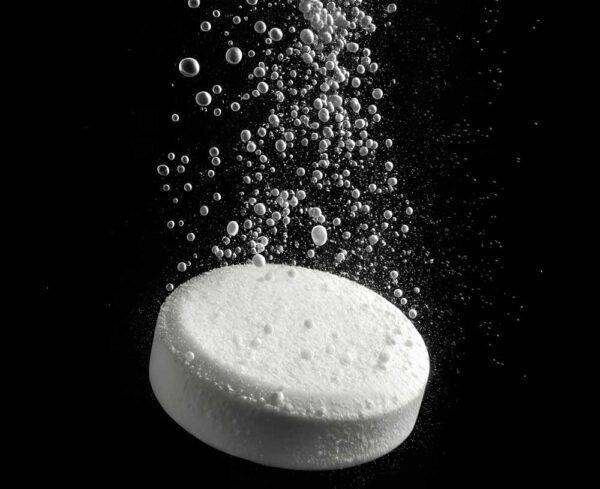 white pill dropped in water resulting in bubbles, black background