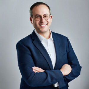 Jeremy Scholem looking into the camera angled slightly to the right with arms crossed and smiling.