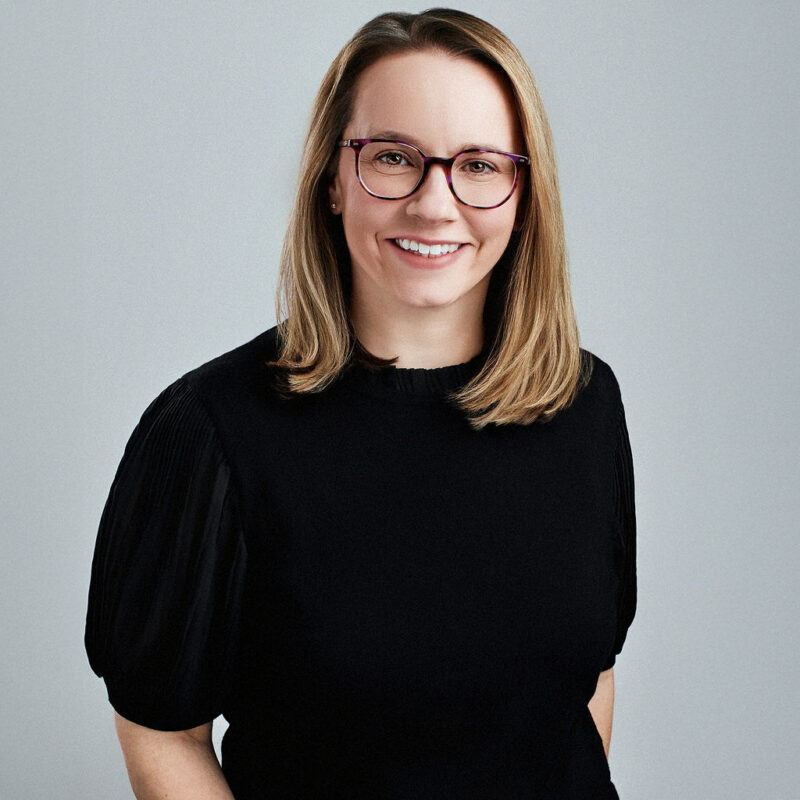 Kathleen Sermabekian looking straight into the camera smiling with arms at her side.