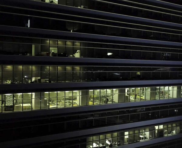 office building at night, windows with blinds open, people working inside