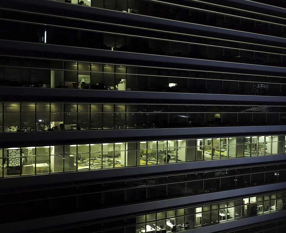 office building at night, windows with blinds open, people working inside