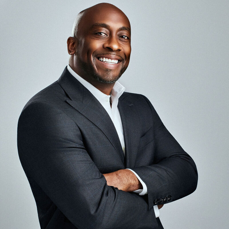 Raymond McLeod looking into the camera smiling angled to the right with arms crossed.