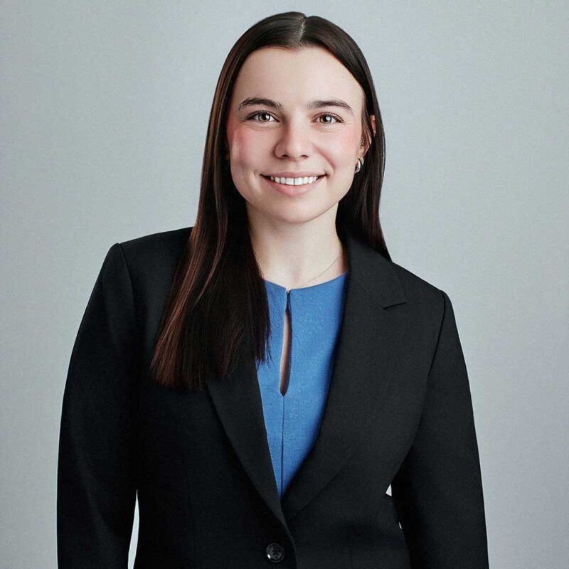 woman standing against a grey background wearing black blazer and blue shit