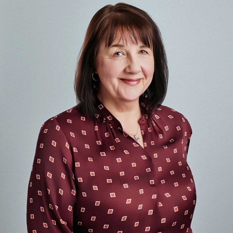woman standing against a grey background wearing a red printed shirt